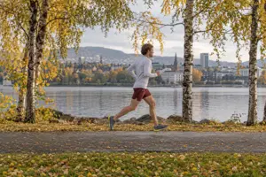 Illustrasjon av en mannlig løper på en asfaltert parksti ved vannet i en norsk by med gule bjørkeblader
